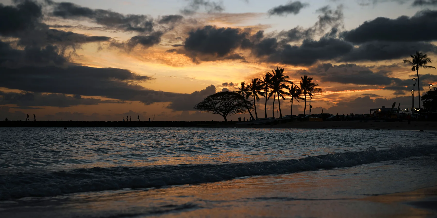 Palm trees silhouetted against an orange and grey sunset sky over the water at Waikiki